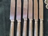 six silverplated knives and five spoons are lined up on a black cloth