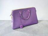 sac à main en cuir violet posé sur une surface en béton, avec un mur blanc en arrière-plan