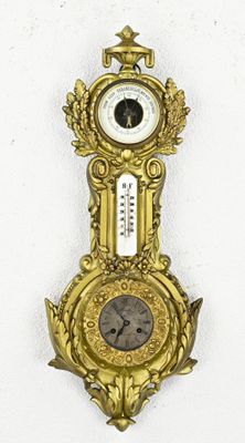 a gold clock hanging on the wall with a thermometer on it
