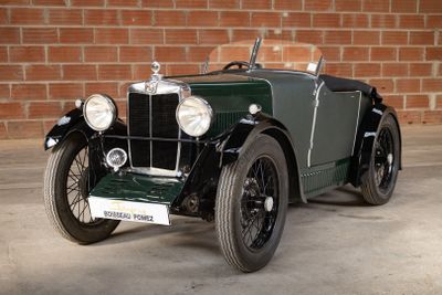 an old green car parked in front of a brick wall