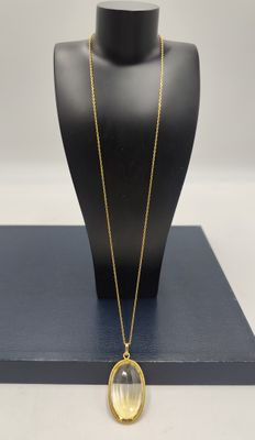 un collier plaqué or avec un pendentif en verre transparent, présenté sur un mannequin