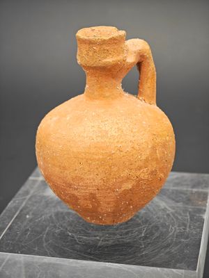 un vase en argile posé sur un socle en verre