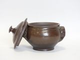 a small brown bowl with a lid on a white surface
