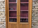 une armoire en bois avec des portes vitrées et des étagères, placée devant un mur en pierre