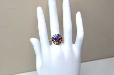 une main blanche tenant une bague sertie de pierres multicolores