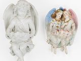 two figurines of angels sitting on a white surface