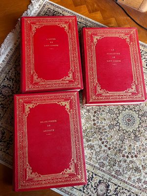 trois livres rouges posés sur un tapis, lui-même posé sur une table en bois