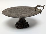a silver plate with a bird on it on a stand