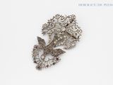 a silver brooch with a bird and flowers on it