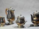 four silver teapots and two silver cups on a table