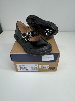 une paire de chaussures en cuir noir avec des boucles, posée sur une boîte en carton