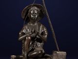 a bronze statue of a boy sitting on a rock with a fishing pole