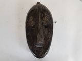 un vieux masque en bois accroché à un mur blanc