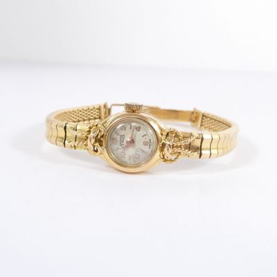 gros plan d'une montre en or sur une surface blanche
