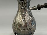 a silver coffee pot with a handle on a stand