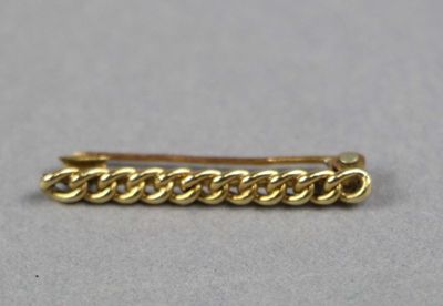 un gros plan d'une broche en forme de chaîne dorée posée sur une surface grise