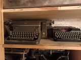 two old typewriters sitting on a shelf in a room