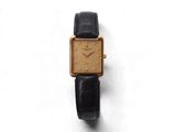 une montre en or avec un bracelet noir posée sur une surface blanche
