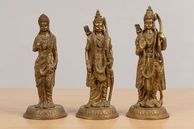 three brass figurines of hindu deities on a wooden table