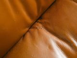 a close up of a brown leather couch with a black cat on it