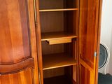 a wooden armoire with shelves and a chair in the corner