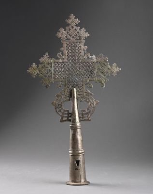 une vieille croix en argent posée sur un vase en argent, sur un fond gris