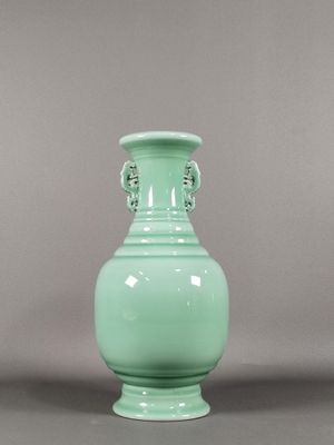 un vase vert posé sur une table, sur fond gris