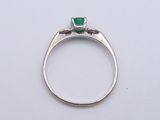 a close up of a diamond and emerald ring on a white surface