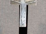 une croix argentée posée sur un socle noir, sur fond gris