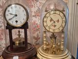 deux horloges posées sur une table recouverte d'une cloche en verre