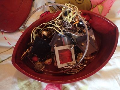 un bol rouge rempli de bijoux variés posé sur un lit