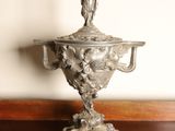 a silver vase with a bird on top of it