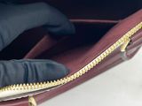 a woman ' s hand holding a red purse with gold zippers