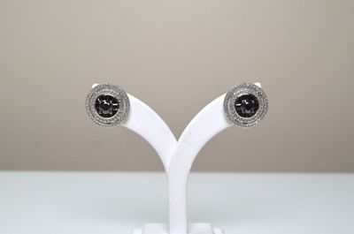 une paire de boucles d'oreilles à clous ornées de diamants noirs et blancs, présentées sur un socle blanc