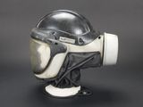 an old black and white helmet on a stand on a black background
