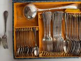 des cuillères, des fourchettes et un repose-cuillère dans une boîte en bois posée sur une surface blanche