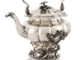 an antique silver teapot with a dragon handle on a stand