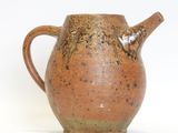 a brown pitcher with a handle on a white surface
