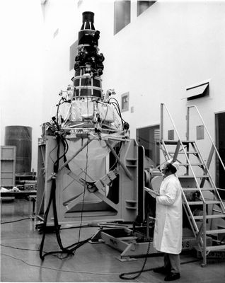 une vieille photo en noir et blanc montrant un homme en blouse de laboratoire debout à côté d'une machine