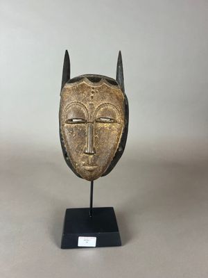 un masque doré muni de cornes, posé sur un socle noir