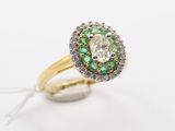 a close up of a diamond and emerald ring on a white surface