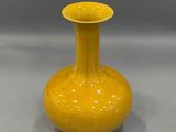 yellow vase sitting on a white surface with a gray background
