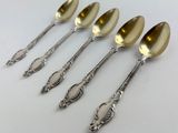 four spoons with a gold handle and a silver spoon on a white surface