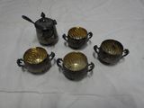 six silver plated teapots and cups with spoons on a white cloth