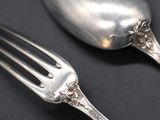 two silver spoons and a fork on a black surface