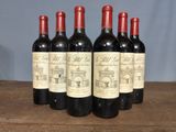 six bottles of red wine are lined up on a wooden table