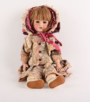 une vieille poupée assise par terre, coiffée d'un bonnet et vêtue d'une robe