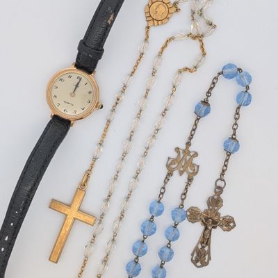 une montre, des bracelets et un chapelet posés sur une table