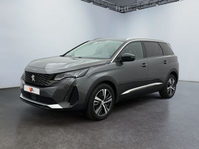 Une voiture grise est garée dans une pièce blanche au sol noir.