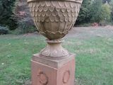 un grand vase en pierre posé sur un socle dans l'herbe
